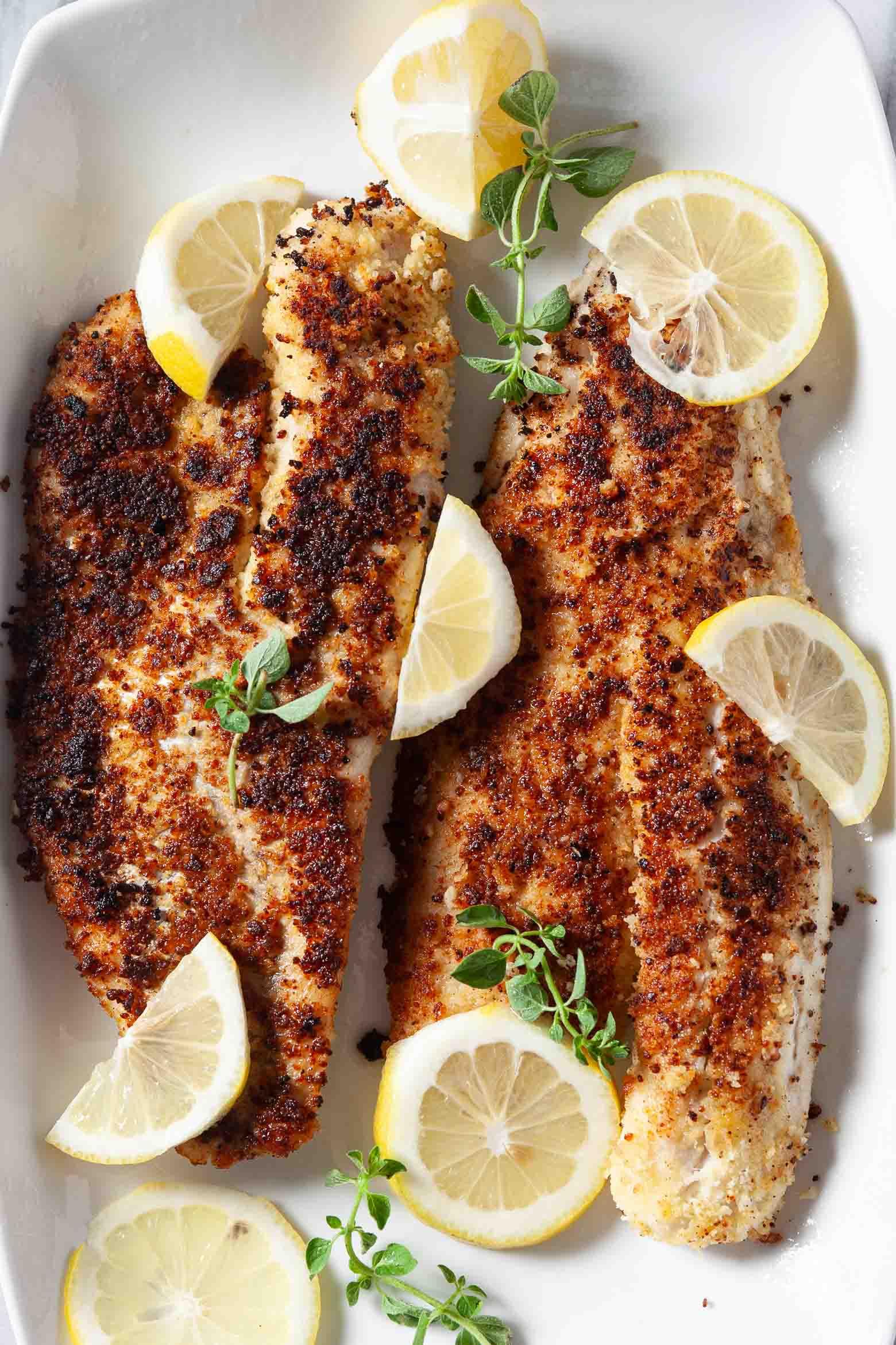 Pan-fried walleye fillets with lemon wedges and fresh herbs on a white platter