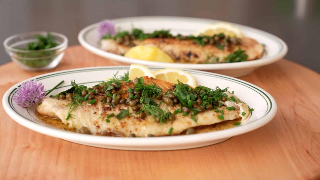 Plated pan-fried walleye fillets with capers, fresh herbs and lemon on a wooden board